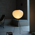 Akari 10D Floor Lamp — lit shade in a dim living room with a lounge chair and concrete floor — Captains Bamboo