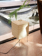 Akari 1X Table Lamp — lit shade on a terrazzo floor beside a tall window with a fern outside — Captains Bamboo
