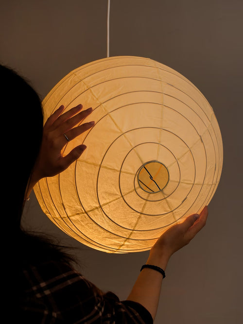 Akari 100D Paper Pendant — a person holding the lit globe, spiral rib rings visible in close-up — Captains Bamboo