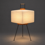 Akari 7A Table Lamp — lit shade glowing warm and spilling light onto a dark studio floor — Captains Bamboo