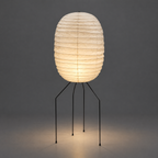 Hitomi Akari UF3-DL Floor Lamp — lit oval shade glowing warm over wall and floor in a dark studio — Captains Bamboo