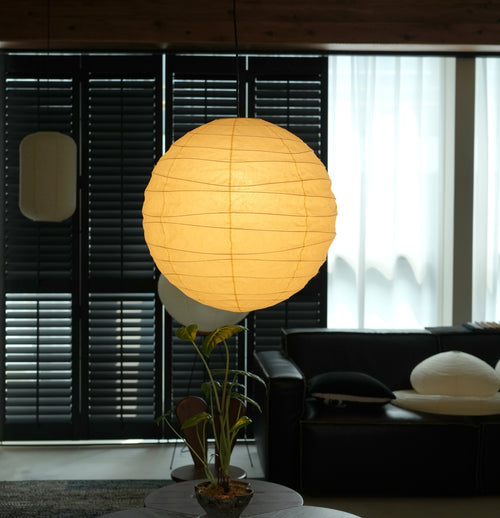 Akari 100D Paper Pendant — large lit globe beside a small round pendant above a plant and sofa — Captains Bamboo