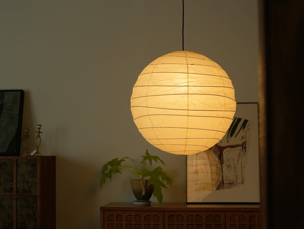Akari 75D Pendant — lit shade glowing above a wooden sideboard with a plant and artwork — Captains Bamboo