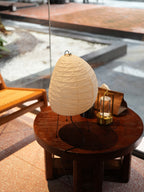 Akari 1N Table Lamp — unlit shade on a round wooden table by a window, rattan chair nearby — Captains Bamboo